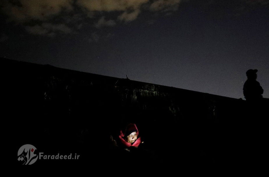 مهاجر آمریکای مرکزی که پشت یک ماشین خالی در قطار باربری نشسته است به سمت مکزیک می‌رود و از نور تلفن همراه خود استفاده می‌کند