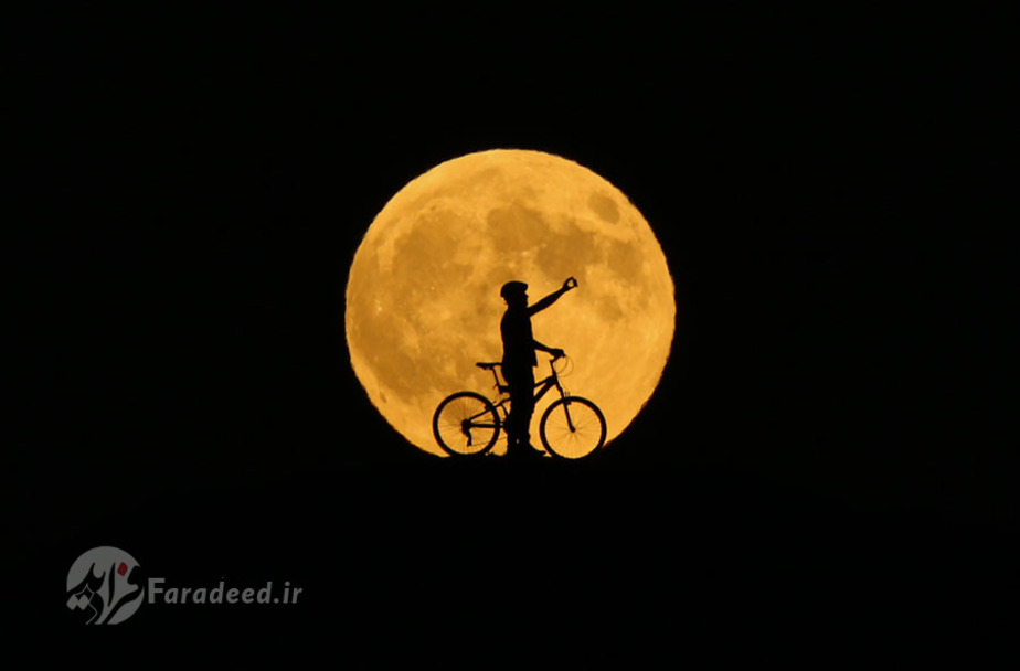 تصویر ماه کامل، پشت مردی که از خود در شهر وان سلفی می‌گیرد.